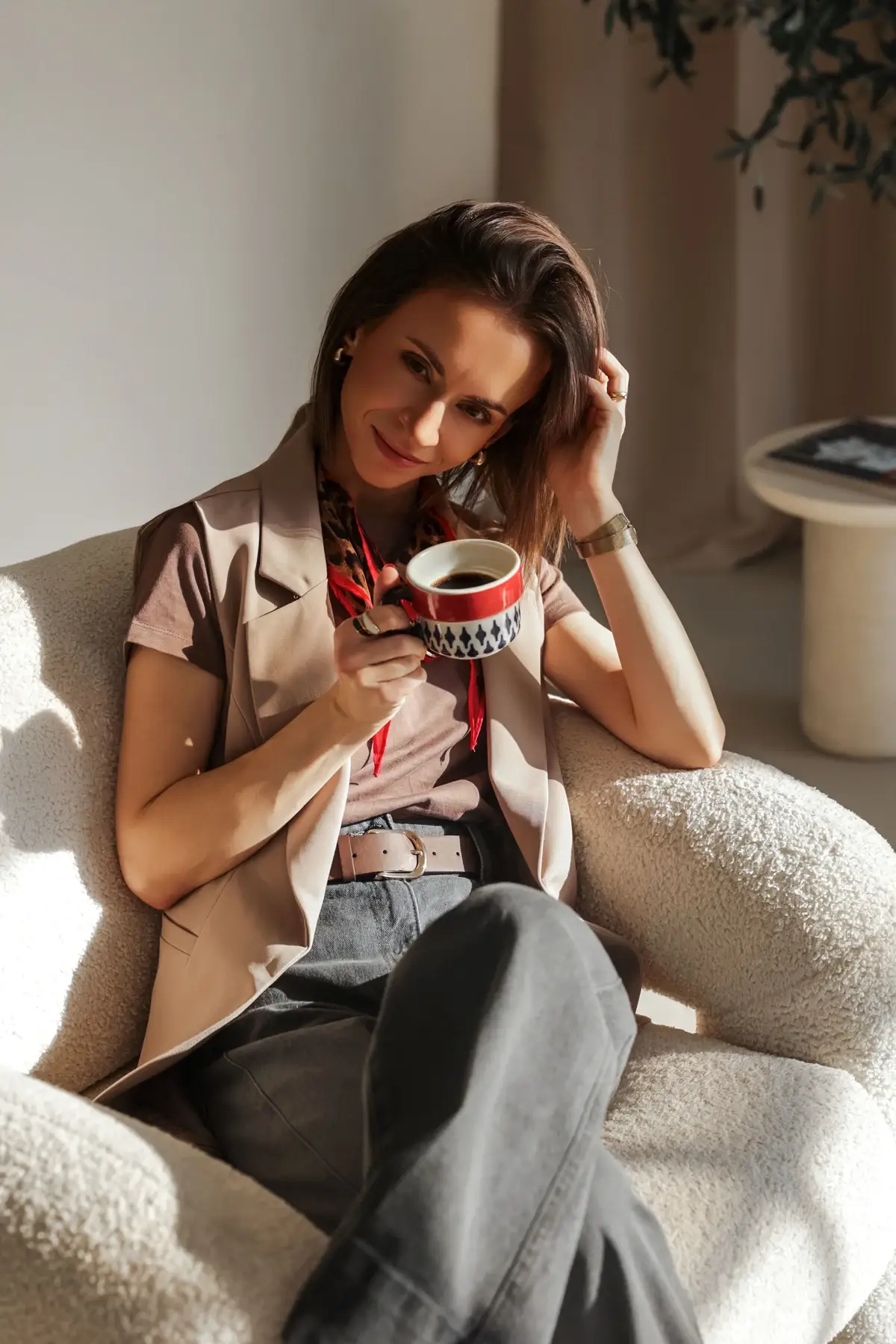 Ewa Smolińska w jasnym wnętrzu, siedzi w białym fotelu z filiżanką w dłoni