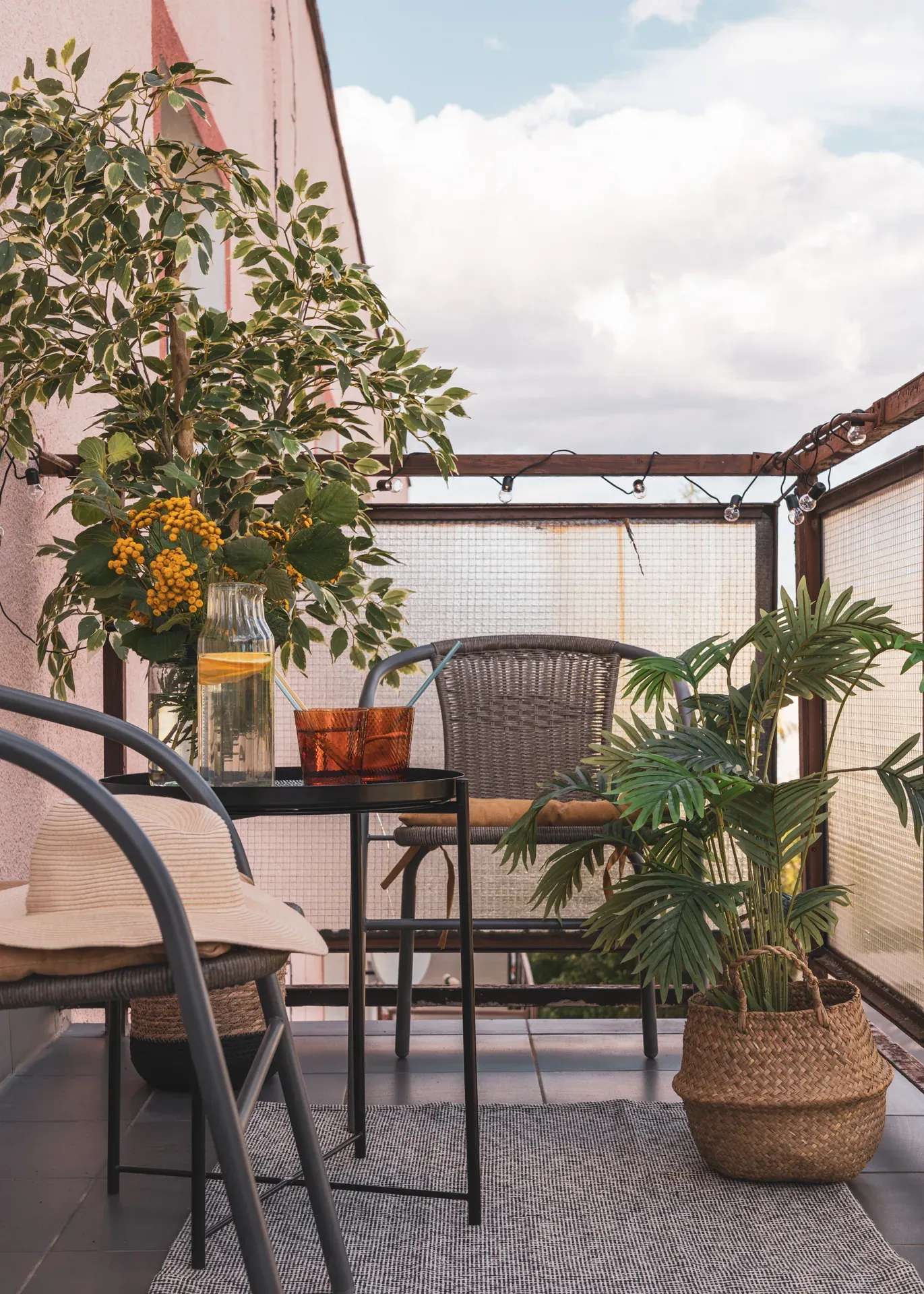 Balkon po home stagingu: krzesła, okrągły stolik z karafką lemoniady i rośliny w koszach