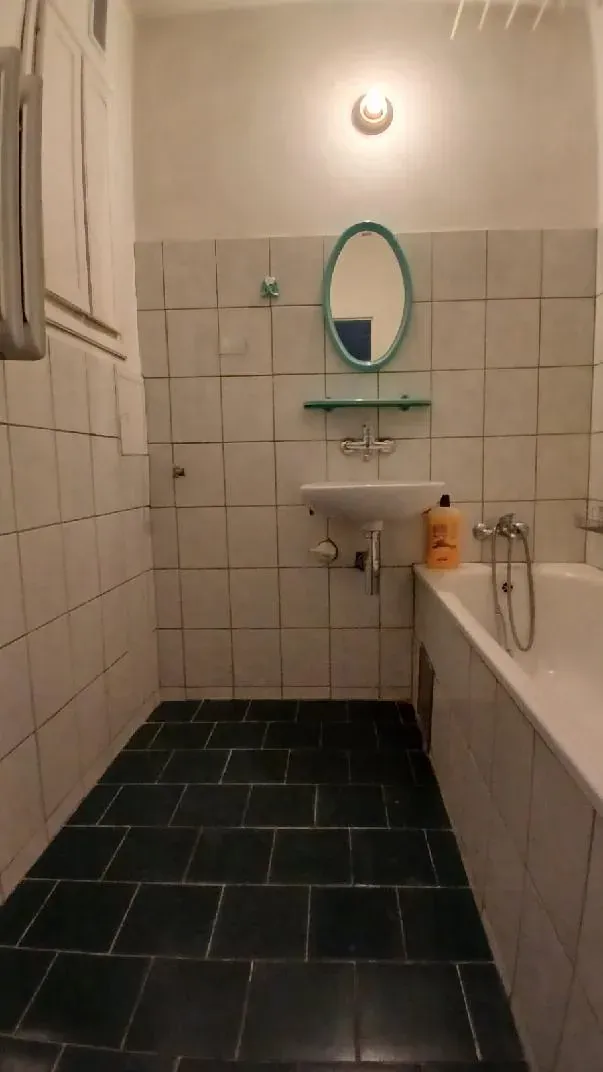 Łazienka przed home stagingiem: stare beżowe kafle, ciemna podłoga, wanna i mała umywalka
