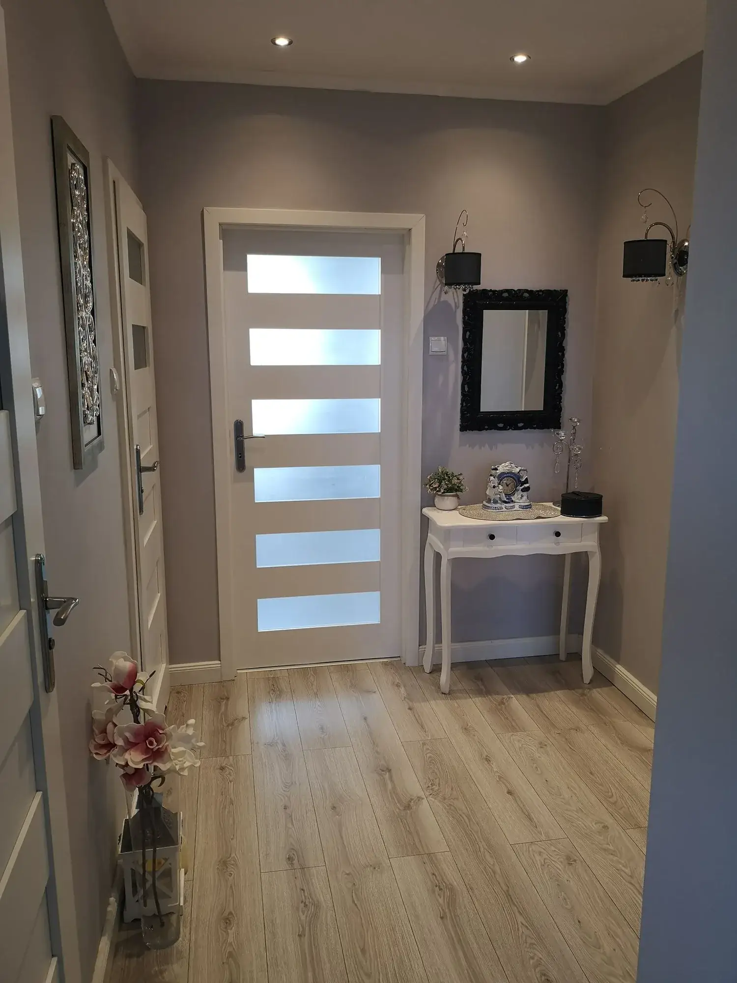 Przedpokój przed home stagingiem: szare ściany, stara biała konsolka z lustrem i obrazami