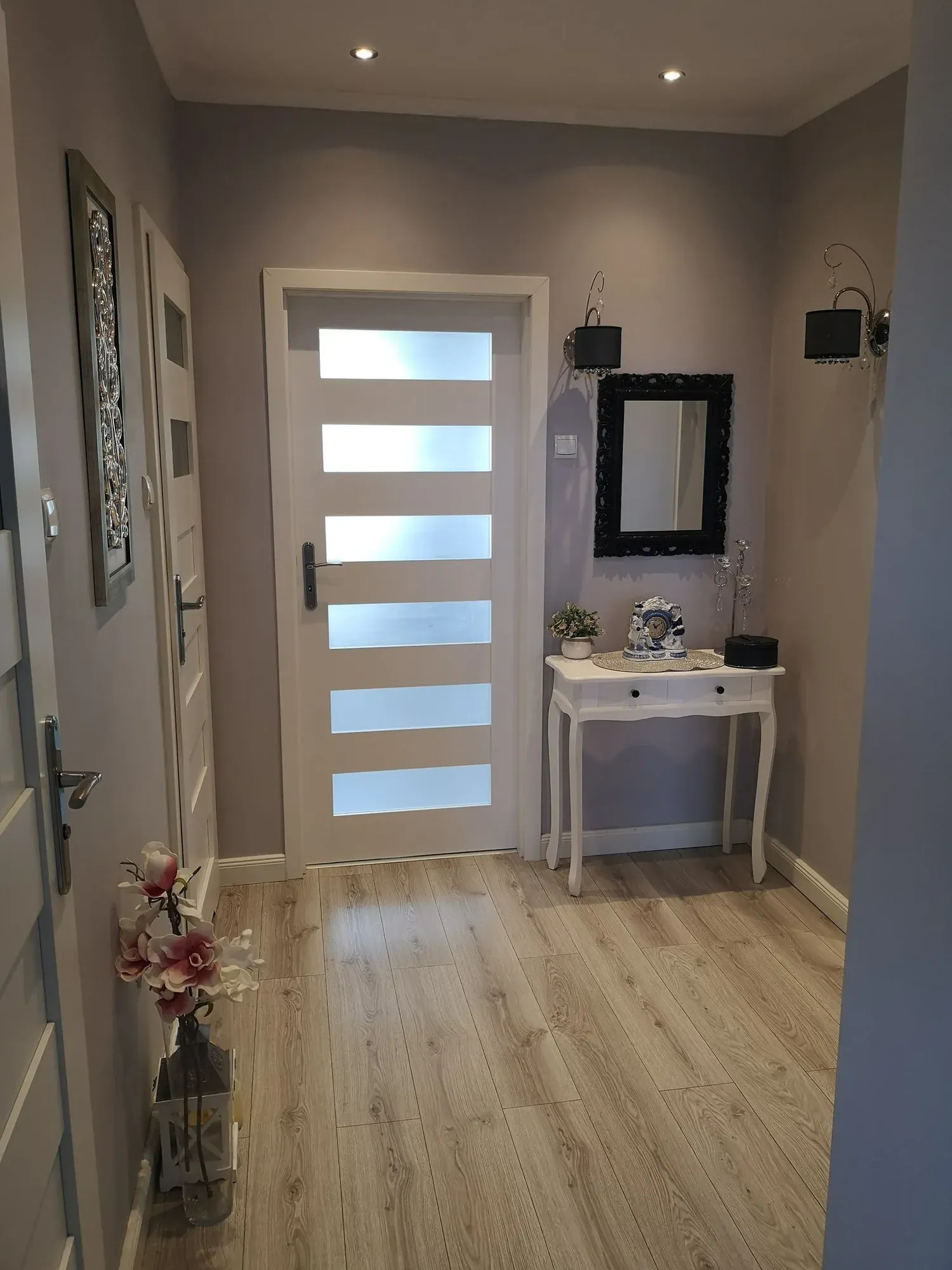 Przedpokój przed home stagingiem: szare ściany, stara biała konsolka z lustrem i obrazami