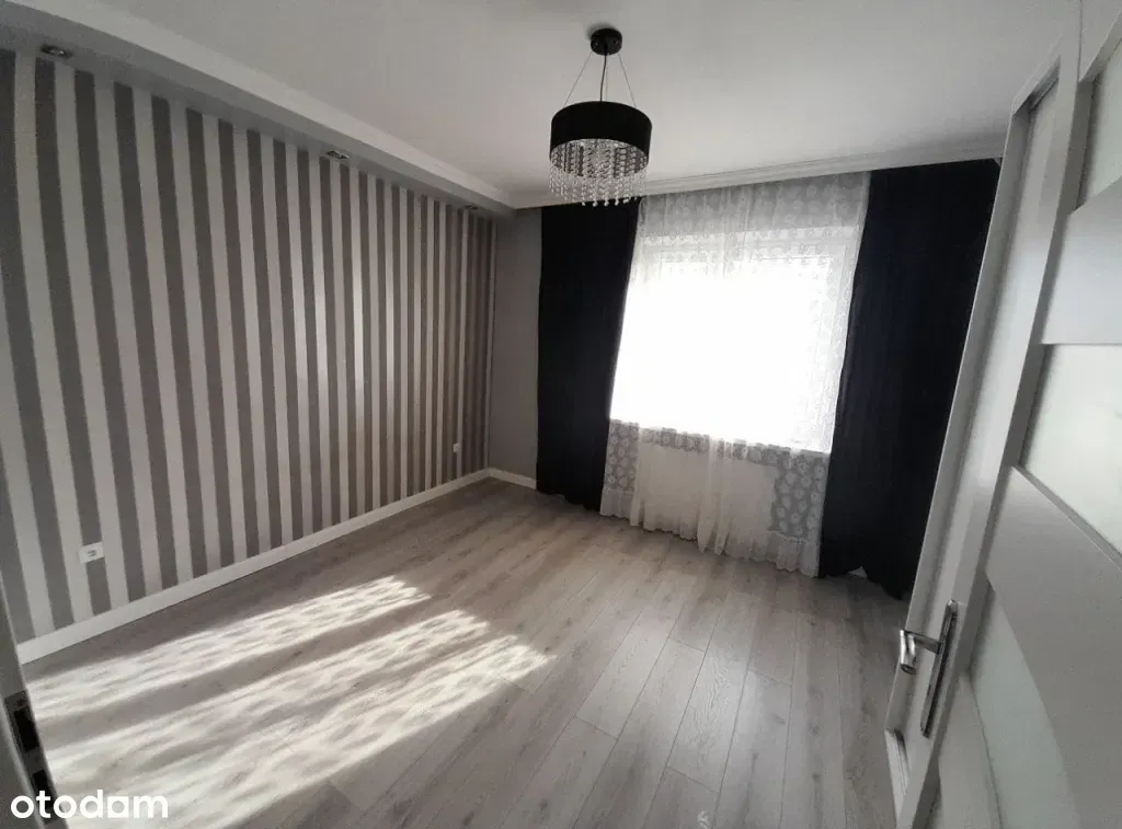 Pusta sypialnia przed home stagingiem: tapeta w szare pasy, ciemne zasłony, firanka i lampa z kryształkami (zdjęcie z ogłoszenia)