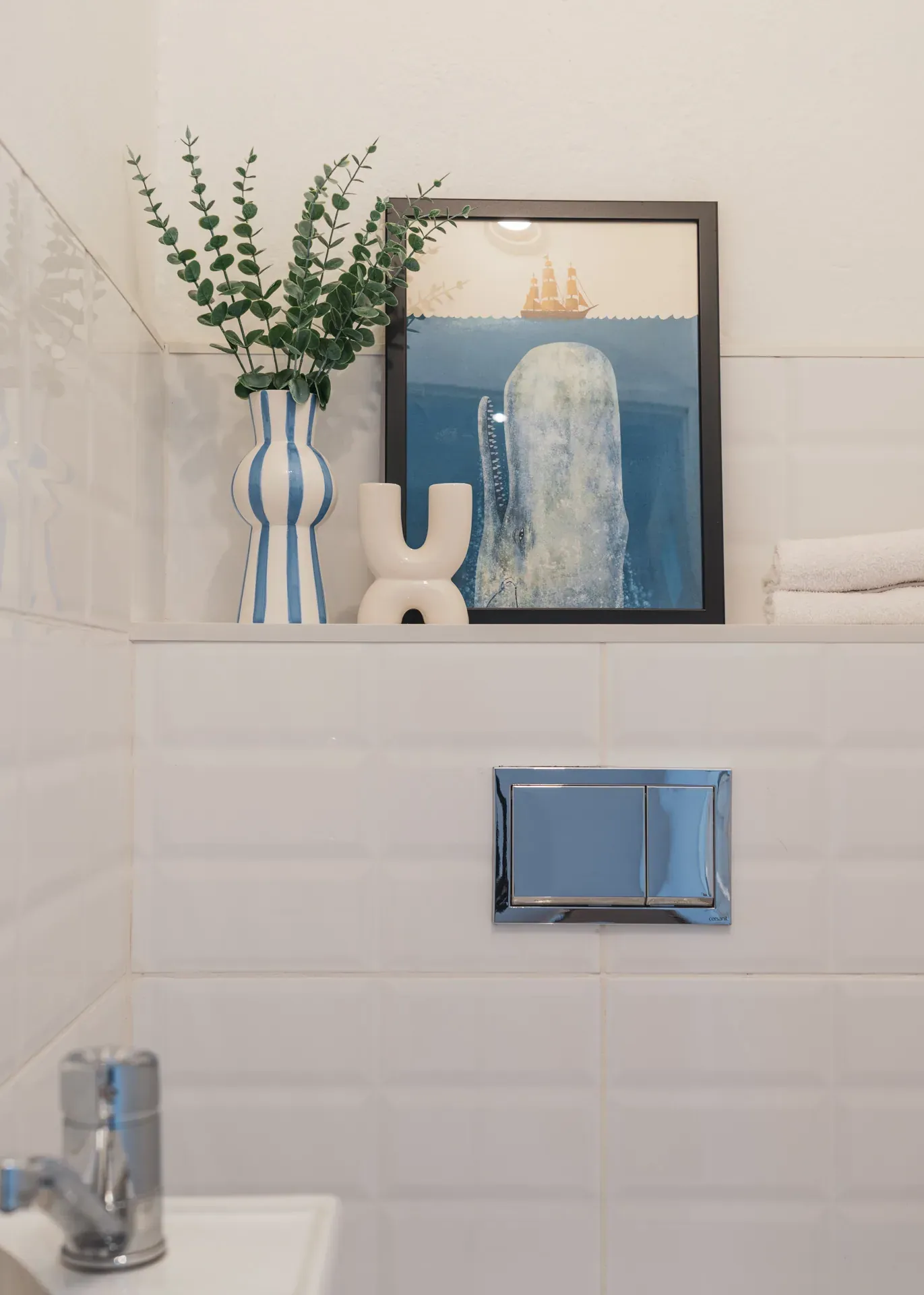 Detal WC: grafika z wielorybem, wazon w paski i ceramiczna dekoracja na półce