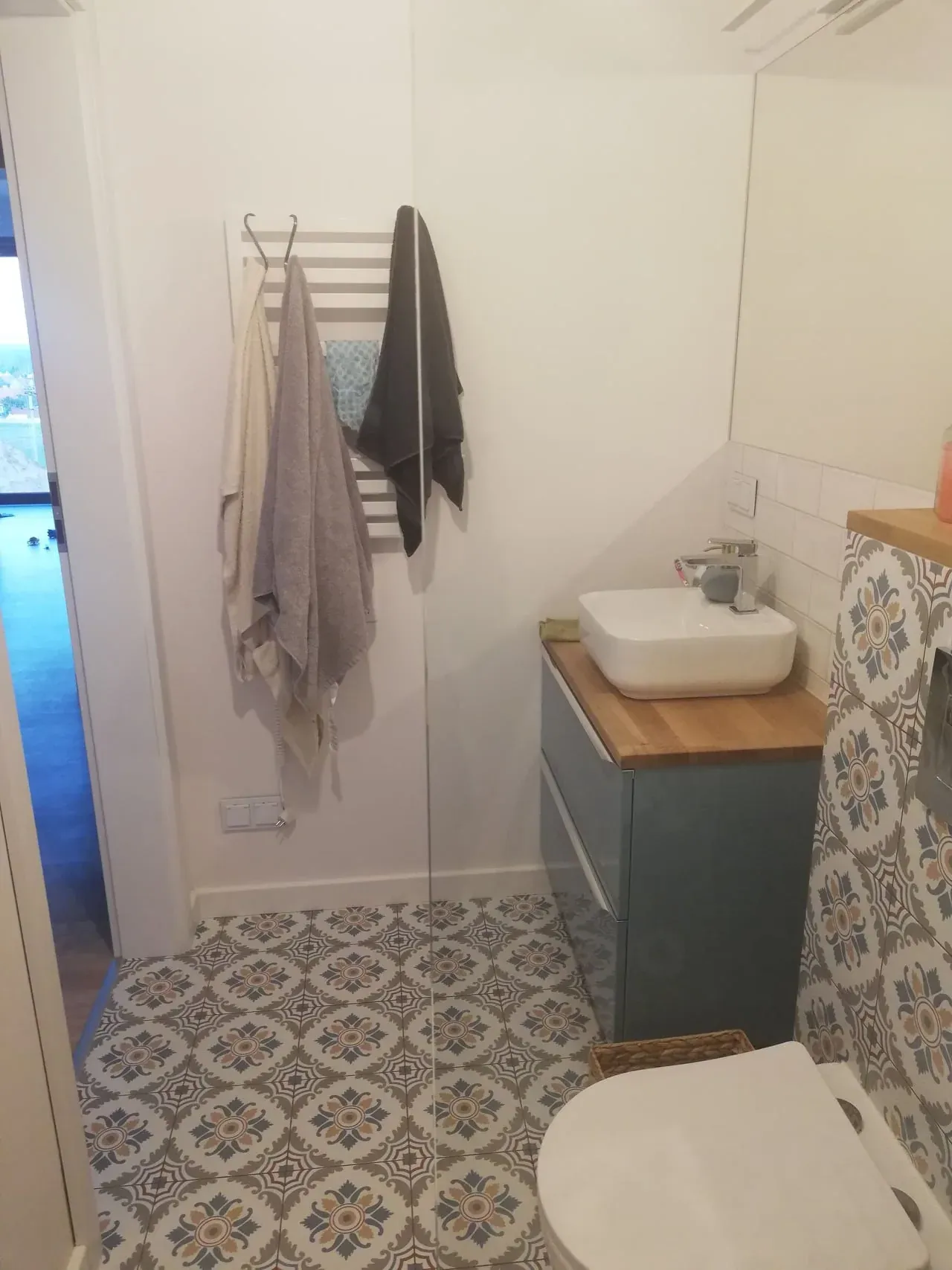 Łazienka przed home stagingiem, widok od drzwi: ręczniki na wieszaku i szafka z umywalką