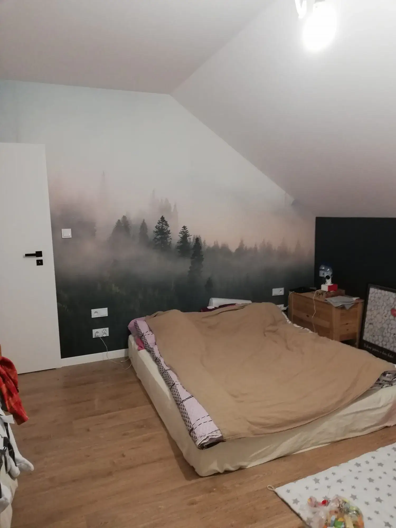 Sypialnia przed home stagingiem: materac na podłodze pod skosem, fototapeta z lasem i rzeczy w nieładzie